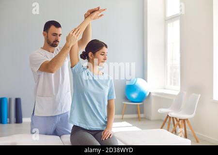Chiropraticien autorisé ou physiothérapeute examinant le bras de la jeune femme dans moderne clinique Banque D'Images