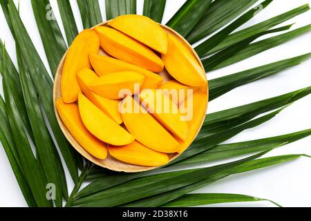 Tranches de mangue sur une assiette en bois sur des feuilles de palmier tropicales. Banque D'Images