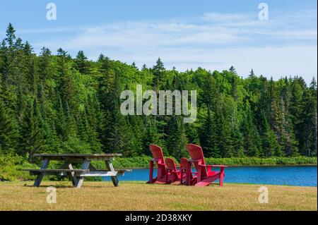 Table de pique-nique et assortiment de quatre chaises Adirondack rouges à un point d'observation sur la rive du lac Wolfe, dans le parc national Fundy, Nouveau-Brunswick, Canada Banque D'Images