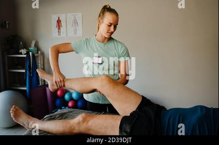Physiothérapeute femme examinant la jambe de son premier patient mâle couché sur un lit pliant dans la salle de conditionnement physique Banque D'Images