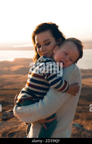 Petit garçon mignon dans les bras de sa mère. Femme à la maison portant son fils nouveau-né. Banque D'Images