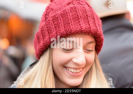 Vue latérale d'un portrait naturel d'un sourire attrayant femme portant un bonnet beanie rouge tricoté en laine dans un gros plan sur la tête Banque D'Images