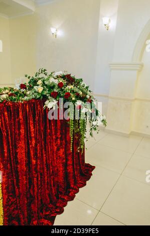 Arrangement de fleurs avec verdure, roses rouges et blanches sur un stand avec un tissu de velours rouge vif dans un hall lumineux. Compositions et détails floraux. Banque D'Images