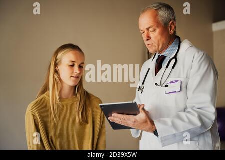 Médecin professionnel effectuant le contrôle et le diagnostic du patient, en tapant sur une tablette numérique et en discutant des résultats avec une patiente Banque D'Images