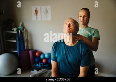 le physiothérapeute féminin effectue un test de cou pour un homme âgé Banque D'Images