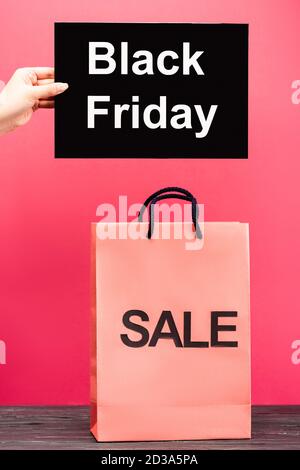 vue rognée de l'affiche de la main féminine avec le vendredi noir lettrage à proximité du sac de shopping sur rose Banque D'Images