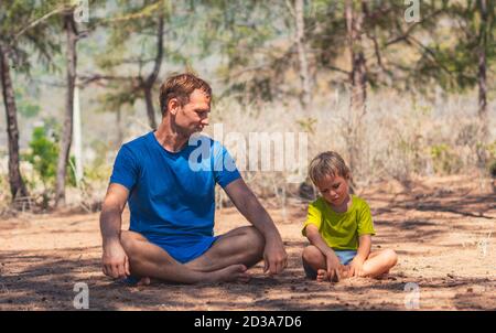 Le père médite la pose de yoga dans le parc forestier à l'air frais, son répète, mais fatigué attendant regarder vers le bas. L'influence de papa sur la vision du monde de garçon. Paternité Banque D'Images