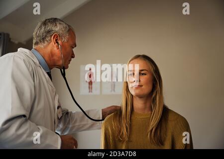 le médecin âgé utilise le stéthoscope pour l'évaluation des jeunes femmes Banque D'Images