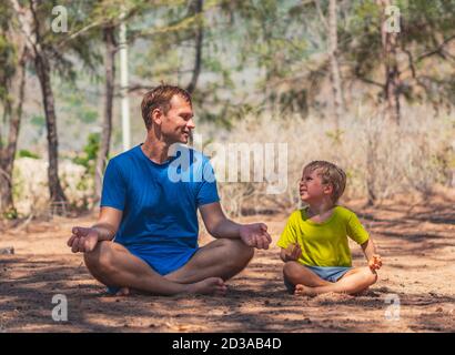 Le père médite la pose de yoga dans le parc forestier sur l'air frais, le fils répète, souriant regard heureux les uns sur les autres. L'influence de papa sur la vision du monde de garçon. Paternité Banque D'Images