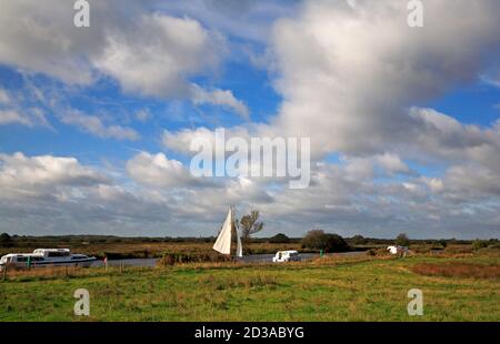 Un yacht de croisière entre les croiseurs sur la rivière Bure sur les Norfolk Broads par le site de l'abbaye de St Benet à Horning, Norfolk, Angleterre, Royaume-Uni. Banque D'Images