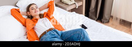 photo panoramique d'une jeune femme se reposant près d'un smartphone avec un blanc écran sur le lit de l'hôtel Banque D'Images