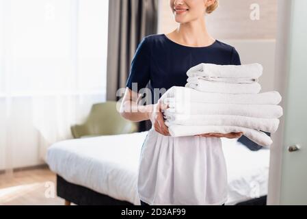 vue courte de la jeune femme de ménage dans un tablier portant des serviettes propres dans la chambre d'hôtel Banque D'Images