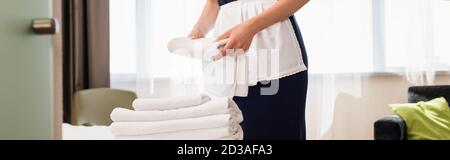vue courte de la femme de ménage dans un tablier tenant une serviette propre dans la chambre d'hôtel, vue panoramique Banque D'Images