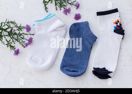 Trois paires de chaussettes et de fleurs pour femmes sur fond blanc structuré, vue du dessus. Banque D'Images