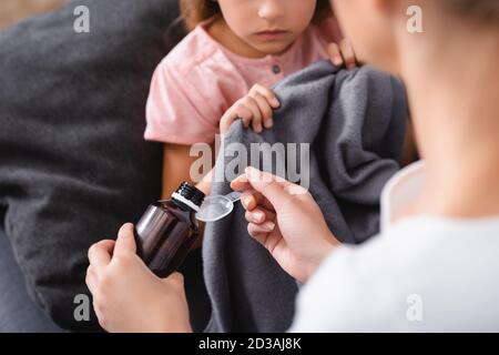 Vue rognée d'une jeune femme qui verse du sirop près d'un enfant malade couverture de maintien à la maison Banque D'Images