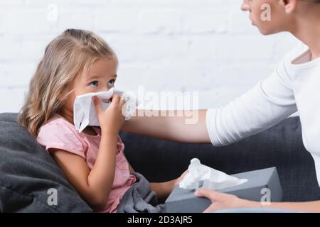 Foyer sélectif de l'enfant malade tenant la serviette pendant le tabac à priser près mère Banque D'Images