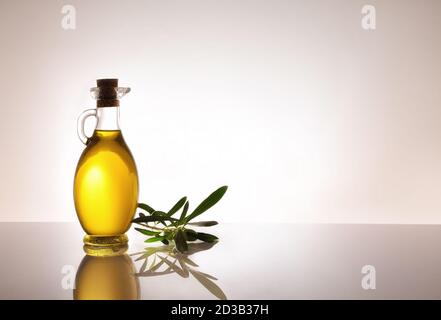 Récipient en verre plein d'huile d'olive rétro-éclairé sur table en verre et fond gris dégradé isolé. Composition à gauche avec espace pour le texte. Banque D'Images