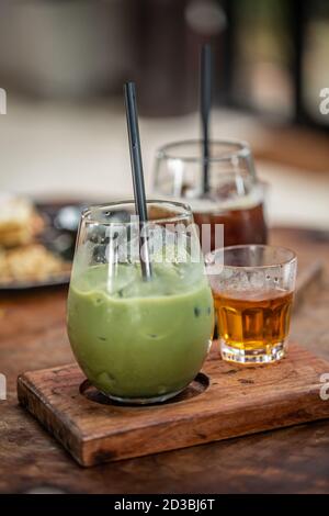 Latte Matcha vert dans une tasse de verre servie avec du thé chaud sur un panneau de bois. Banque D'Images