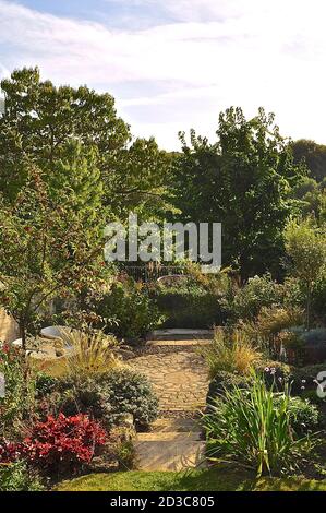 Bien établi traditionnel anglais cottage jardin avec des lits de fleurs matures bien approvisionnés et cadran solaire en pierre. Banque D'Images