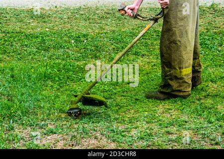 les vêtements d'homme au travail tond l'herbe verte avec un coupe-herbe Banque D'Images
