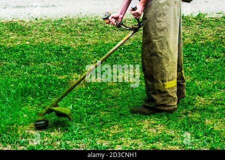 les vêtements d'homme au travail tond l'herbe verte avec un coupe-herbe Banque D'Images