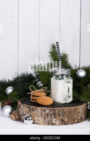 Scène de la vie de Noël. Bougie parfumée dans un pot en verre et biscuits sur une épaisse bûche en bois près d'une branche d'épicéa avec boules de Noël sur un W blanc Banque D'Images