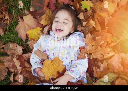 Sourire heureux enfant dans la pile de feuilles jaunes au-dessus de la vue de dessus Banque D'Images