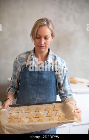 Femme blonde portant un plateau de maintien bleu avec des biscuits de sapin de Noël. Banque D'Images