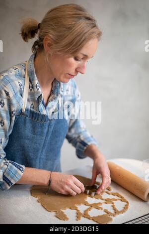 Femme blonde portant un tablier bleu coupant les biscuits de Noël. Banque D'Images