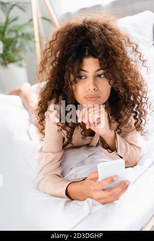 femme mécontentait de se coucher sur le lit et de tenir un smartphone dans la chambre Banque D'Images