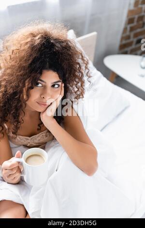 vue en grand angle de la jeune femme maurique tenant une tasse de café dans le lit Banque D'Images