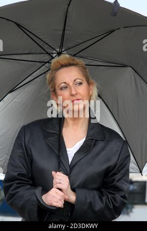 Blanc blanc blanc blanc blanc teint blond femme d'âge moyen dans ses 40 ans portant une veste de manteau en cuir achetée dans une deuxième boutique de main. Sourire avec un parapluie Banque D'Images