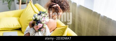 image horizontale de la jeune femme avec les yeux fermés tenant le bouquet et sentant des fleurs dans le salon Banque D'Images