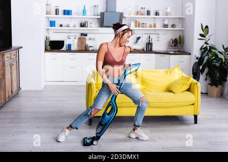 Femme au foyer avec aspirateur imitant jouer de la guitare à la maison Banque D'Images