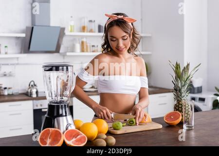 Foyer sélectif de la jeune femme coupant le kiwi tout en préparant le smoothie dans la cuisine Banque D'Images