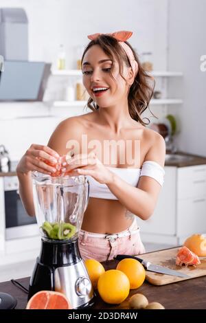 Foyer sélectif de la femme ajoutant des fruits dans le mélangeur tout en faisant smoothie dans la cuisine Banque D'Images