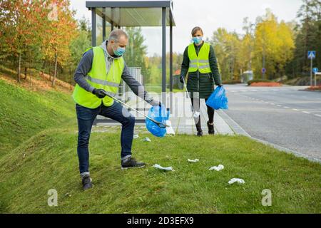 Les ordures du coronavirus. Les bénévoles collectent des masques et des gants médicaux jetables usagés près de l'arrêt d'autobus et le long de la route. Problèmes environnementaux Banque D'Images