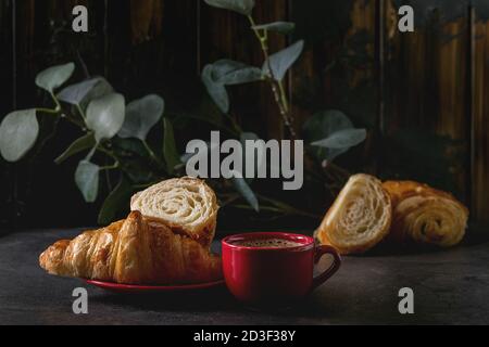 Tout frais cuit et tranché un croissant rouge avec tasse de café espresso sur tableau noir à l'eucalyptus. Style rustique foncé Banque D'Images