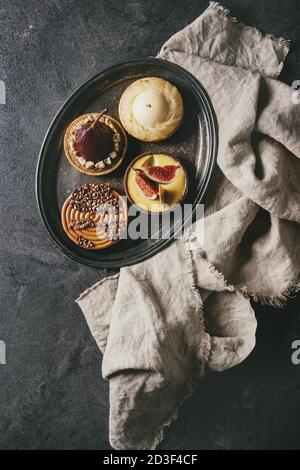 Variété de sweet tartelettes au chocolat, caramel, poires, figues sur vintage plateau avec tissu sur fond texture noire. Mise à plat, de l'espace Banque D'Images