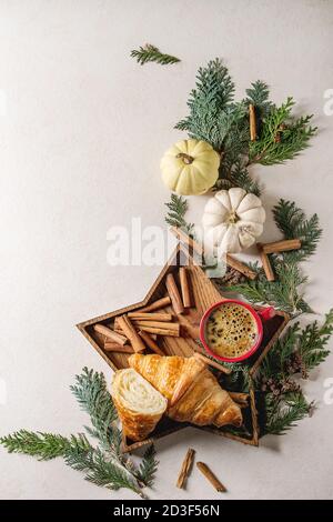 Croissant entières et tranchées, rouge tasse de café espresso dans star shape plateau en bois avec des bâtons de cannelle, blanc citrouilles et thuja branches ov Banque D'Images