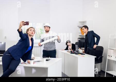 Les employés qui s'amusent au bureau, se posent, font des visages bizarres et prennent des selfies avec un smartphone. Banque D'Images