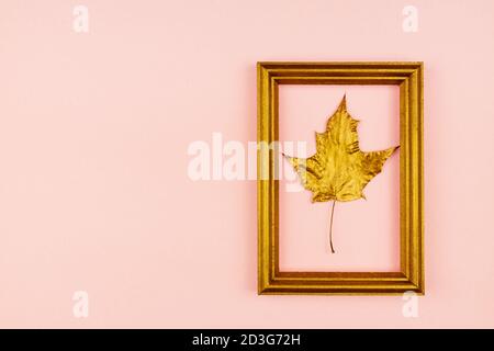 f feuilles d'érable dorées et cadre photo en bois sur fond rose. Concept tendance. Pose en flanelle dans un style minimaliste Banque D'Images