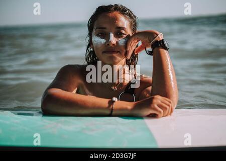 Portrait d'une jeune surfeuse européenne avec ses mains sur sa planche de surf