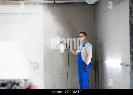 Travailleur à l'atelier de lavage de voiture, utilisant un nettoyeur à pression sur la voiture, homme lavant la voiture avec une mousse. Banque D'Images