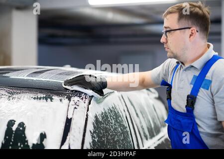 L'homme après le lavage essuie la voiture noire avec un chiffon au lavage de voiture. Main mâle et carrosserie de voiture de près. Banque D'Images