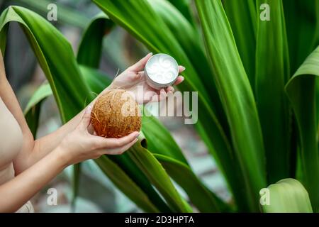 Gros plan des mains des femmes tenant une noix de coco et un pot de crème Banque D'Images