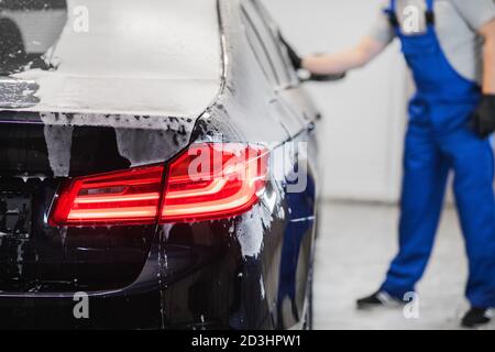 L'homme après le lavage essuie la voiture noire avec un chiffon au lavage de voiture. Main mâle et carrosserie de voiture de près. Banque D'Images