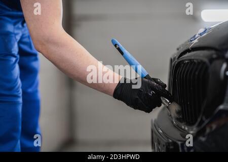 Gros plan de l'homme main dans des gants de protection noirs nettoyage de la grille de radiateur avec une brosse spéciale. Lavage de voiture et service d'habillage. Banque D'Images