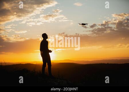 Silhouette d'un jeune homme utilisant un drone dans UN Cadre rural au coucher du soleil Banque D'Images