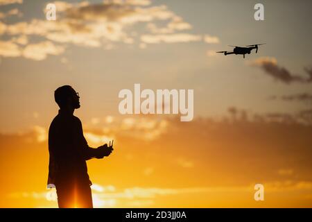 Silhouette d'un jeune homme utilisant un drone dans UN Cadre rural au coucher du soleil Banque D'Images